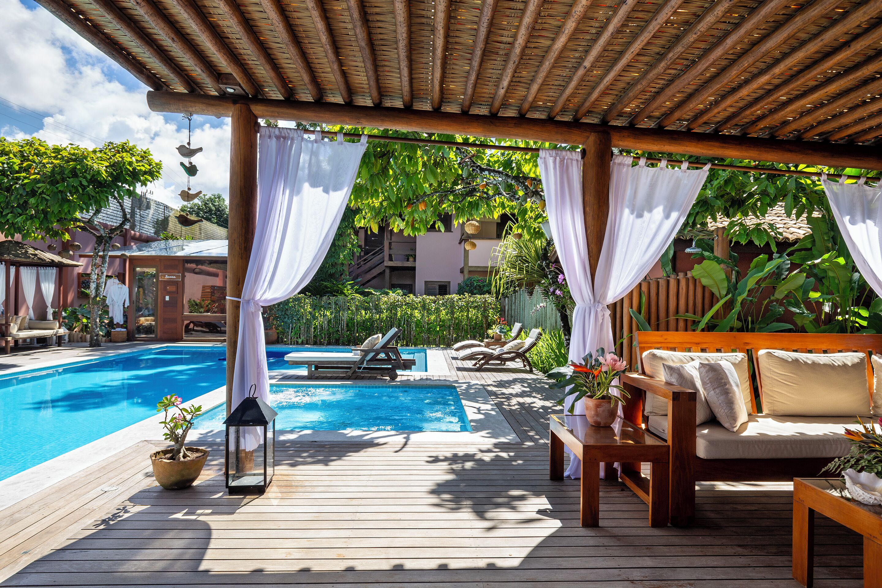 Una terraza de madera con piscina, un sofá y una mesa con un farol.