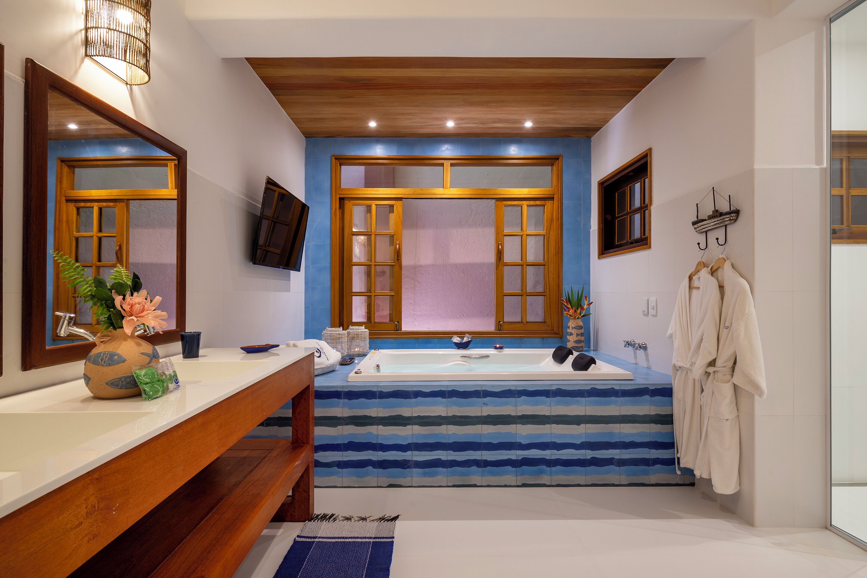 Une salle de bain avec un meuble-lavabo en bois, un grand miroir, une baignoire et un peignoir suspendu à un porte-serviettes.