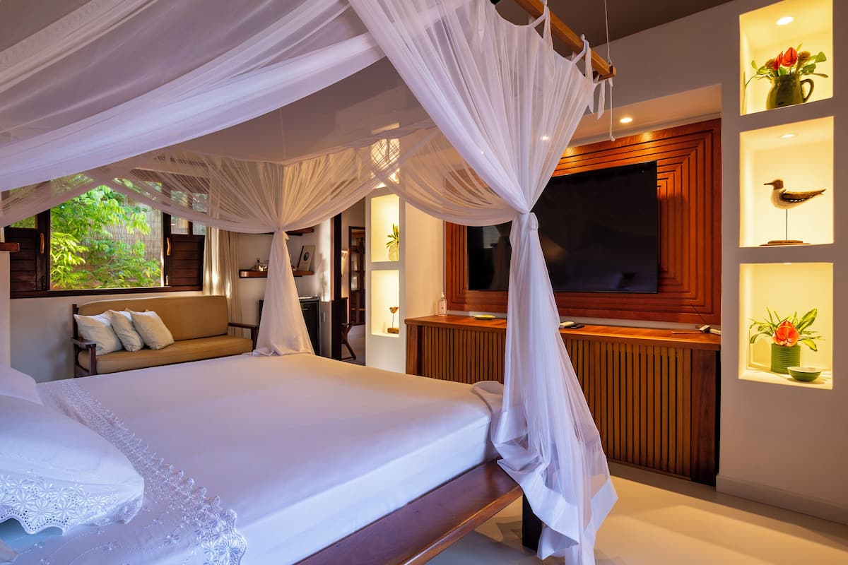 A bedroom with a canopy bed, a wooden dresser, a television, and decorative shelves with flowers.
