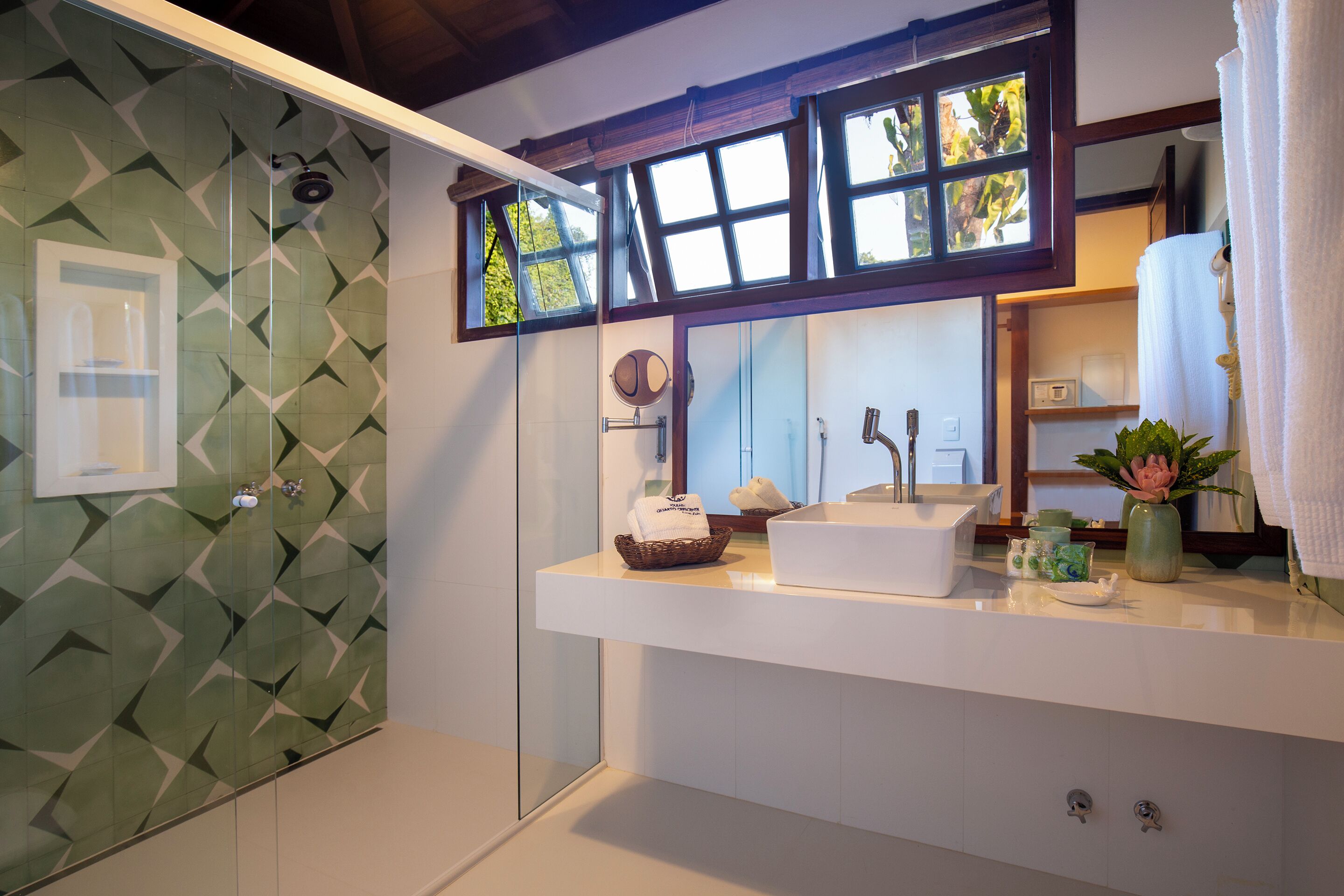 A bathroom with a geometric tile backsplash, a white sink with a mirror above it, and a window with a view of greenery.