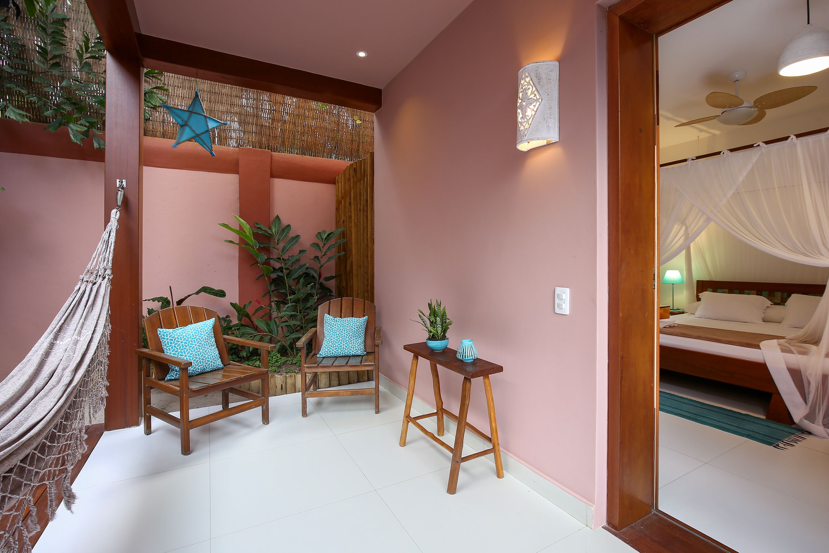 Una habitación con una cama, una silla de madera, una mesita pequeña y una hamaca.