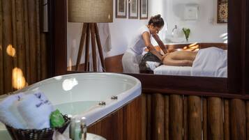 A spa room with a wooden wall, a large mirror, a massage table, and a bathtub.