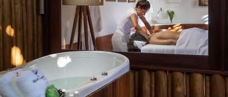 A spa room with a wooden wall, a large mirror, a massage table, and a bathtub.