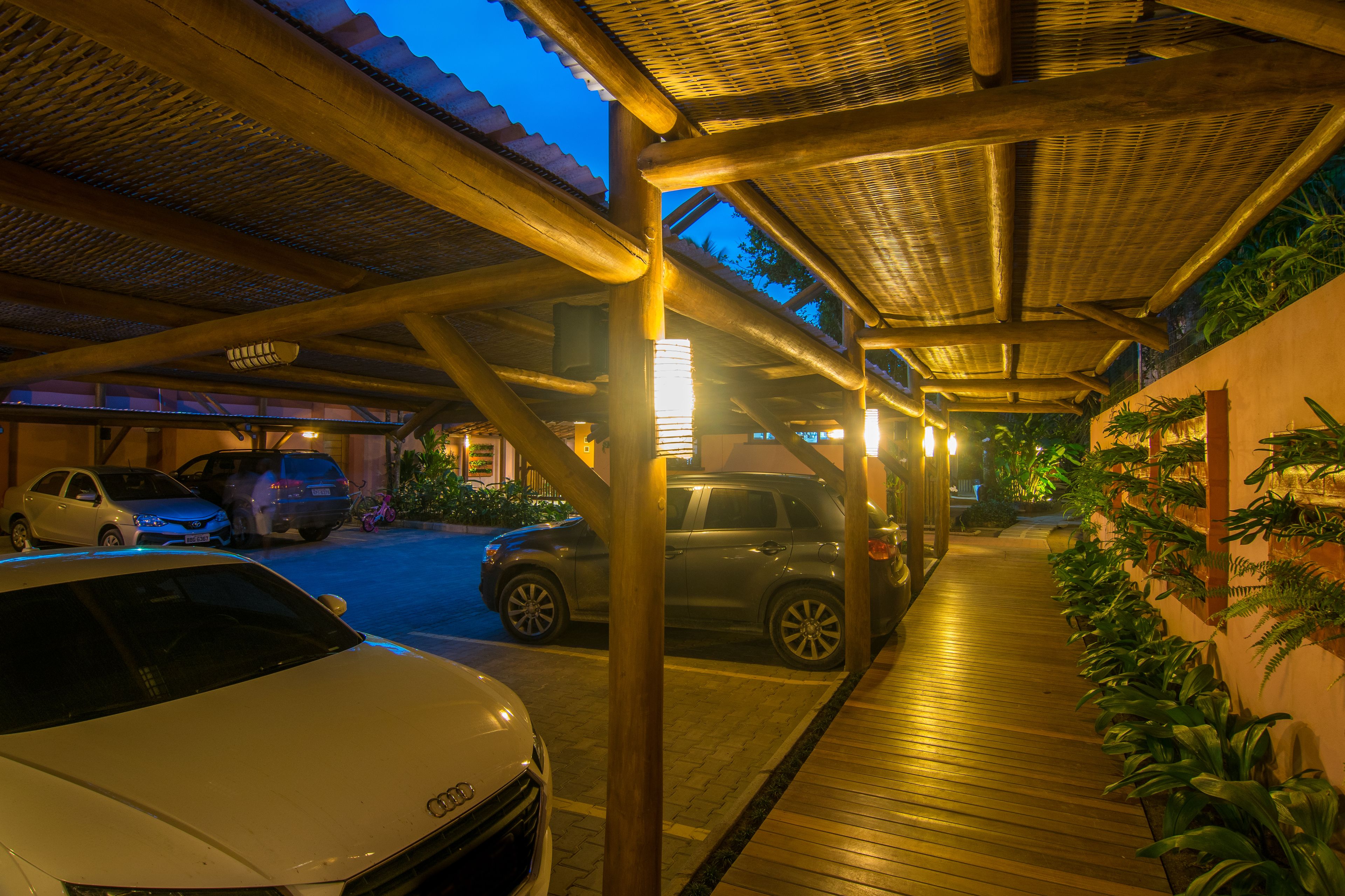 A covered parking area with vehicles, a wooden walkway, and potted plants.