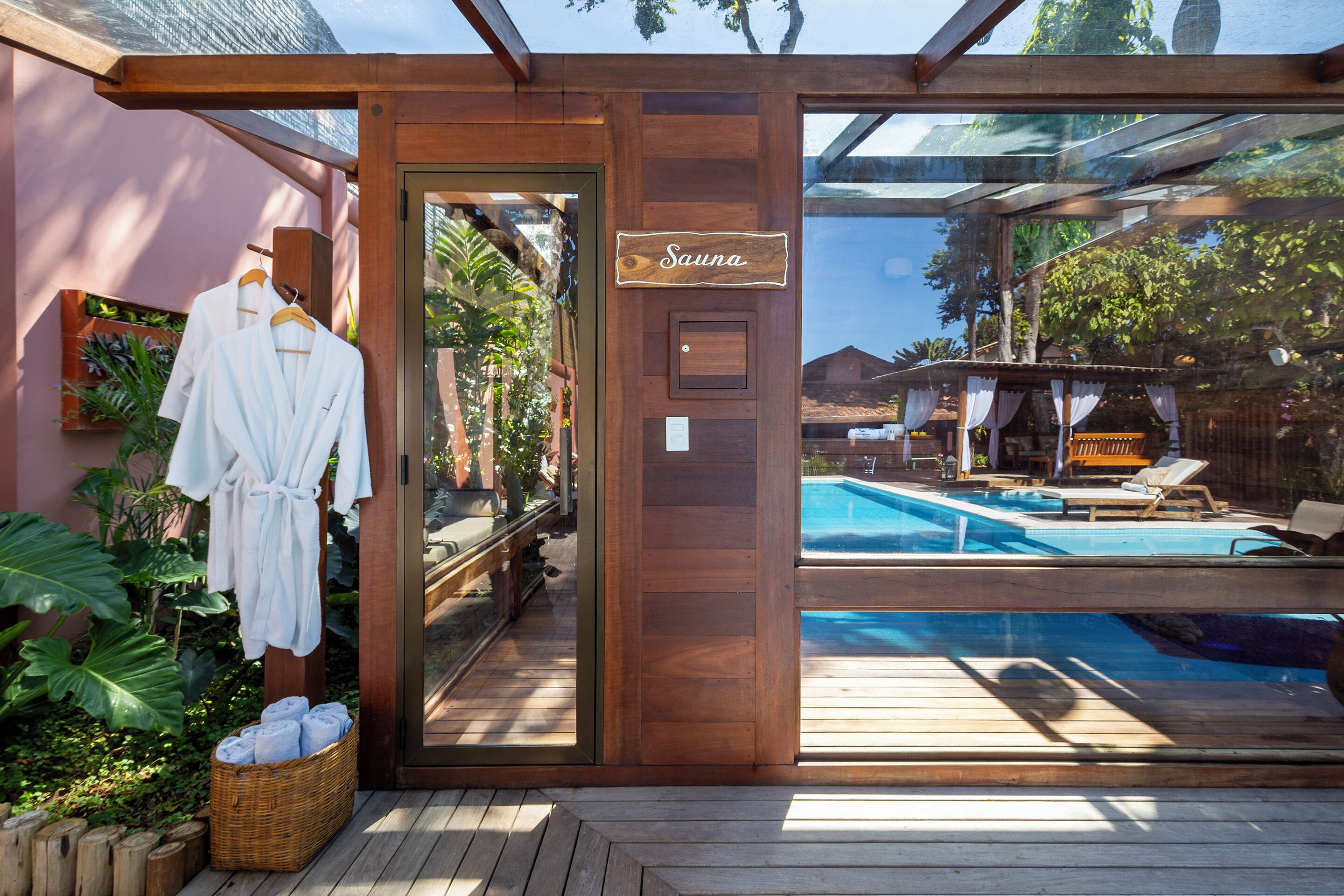 A wooden sauna entrance with a sign, a pool area with lounge chairs, and a basket of towels.