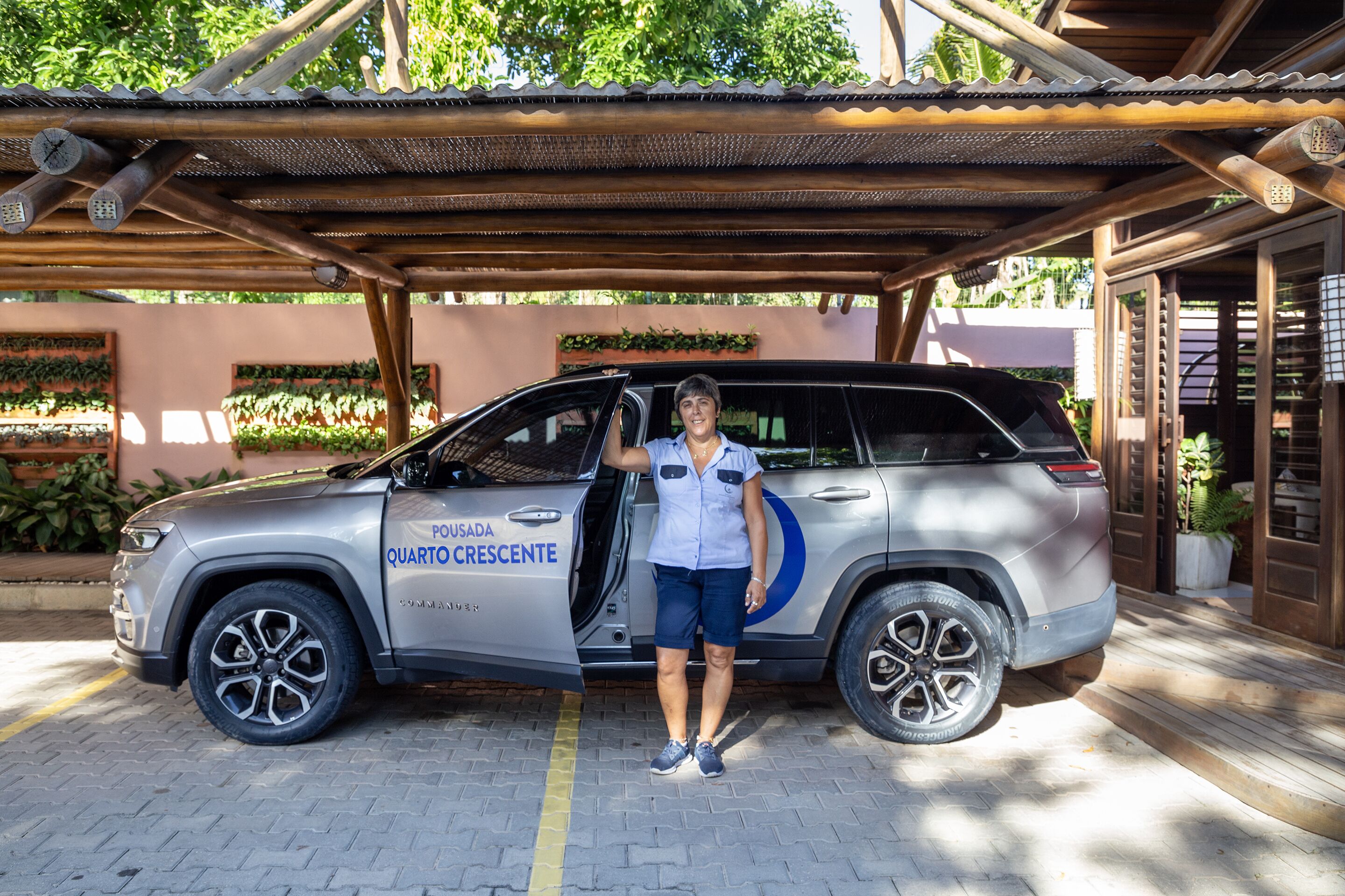 Un SUV plateado con la leyenda "PONSA DA QUARTO CRESCENTE" en la puerta, estacionado bajo una pérgola de madera con suelo de baldosas.