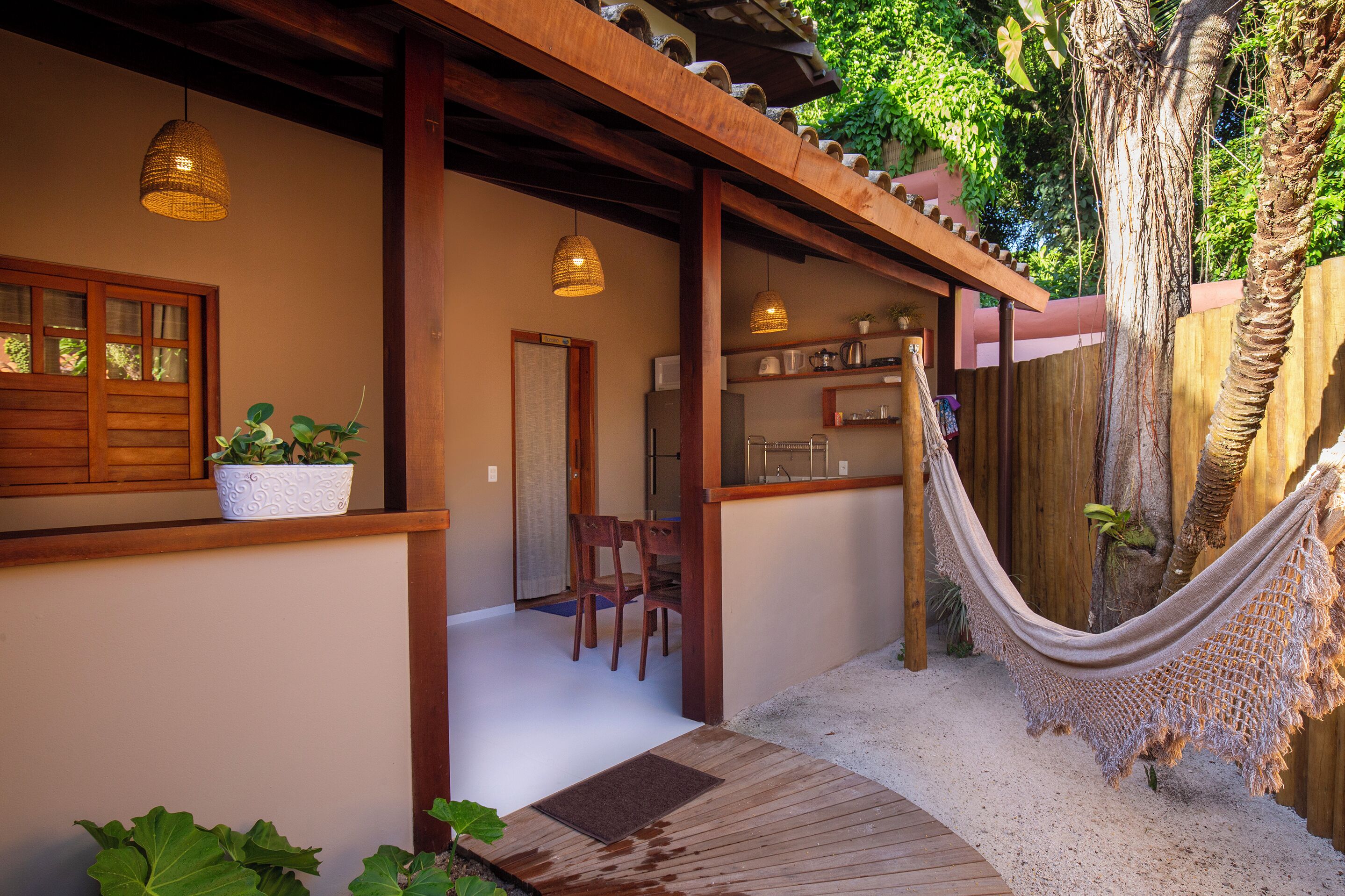 Una terraza de madera con una hamaca, una planta en maceta y un banco de madera.
