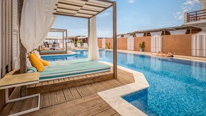 Uma área à beira da piscina com um deck de madeira, um espaço de estar coberto com um toldo branco e uma piscina.