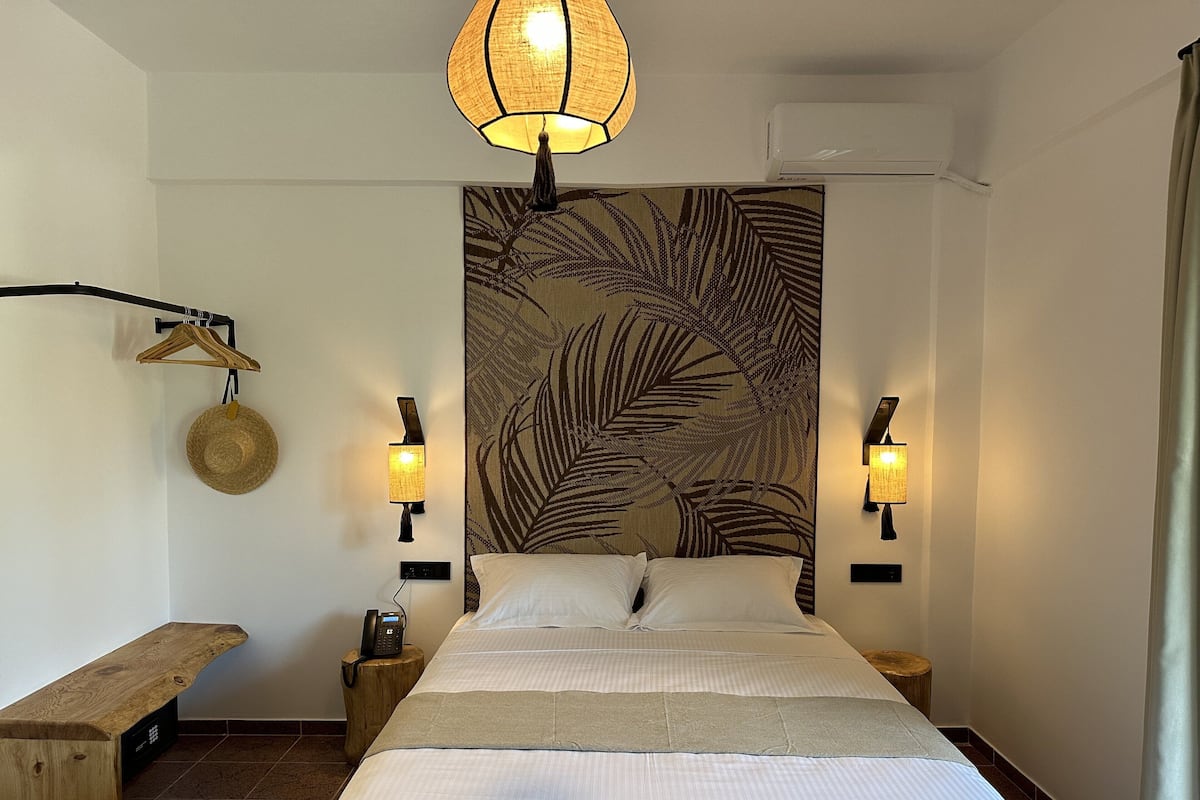 A bedroom with a bed, two bedside lamps, a hanging hat, a wooden bench, and a wall-mounted phone.