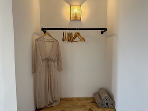 A room with a wooden floor, a hanging garment rack with clothes, and rolled towels on the floor. - Armeno Resort and Armeno Annex (Corfu)