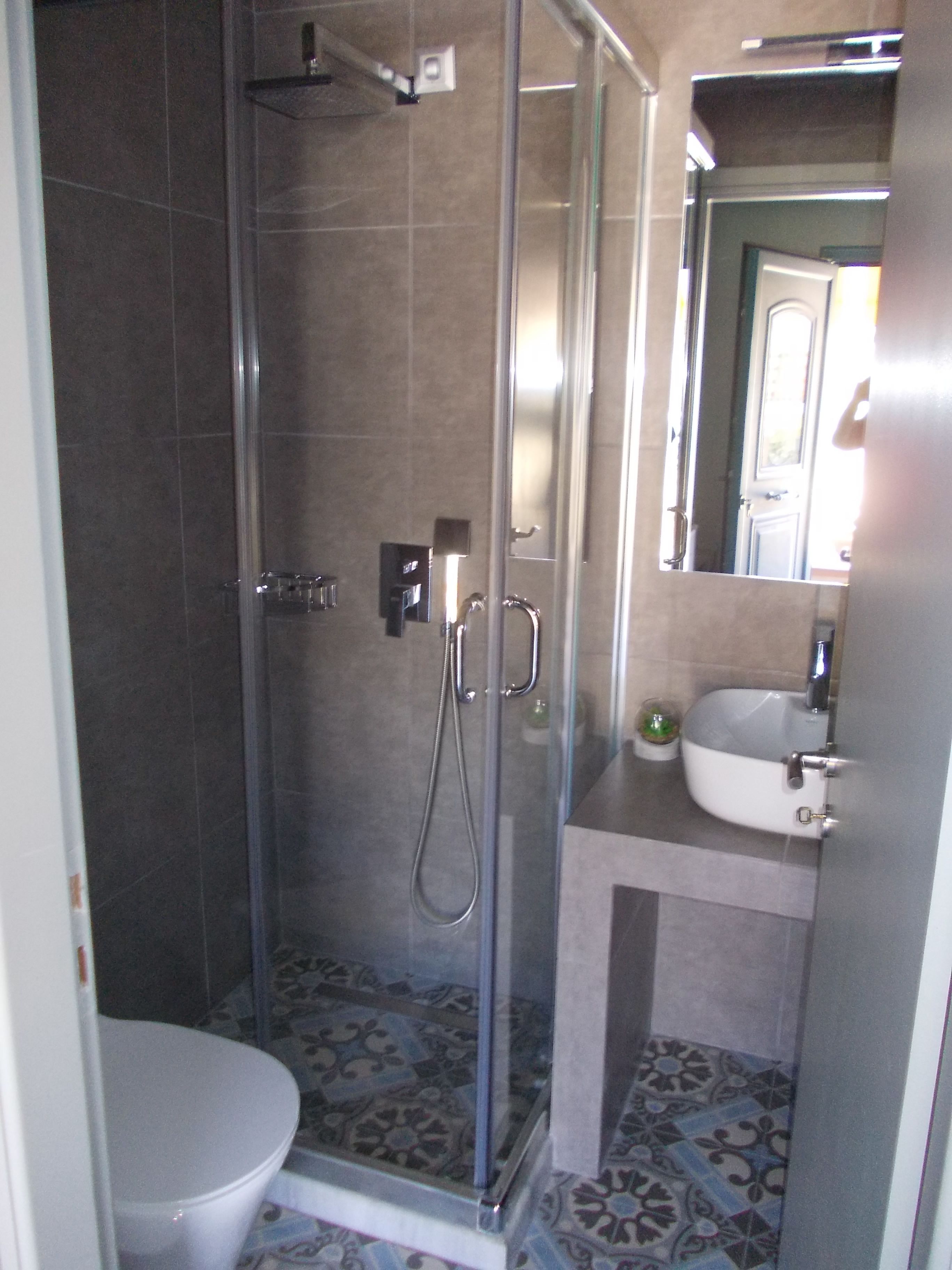 A bathroom with a glass-enclosed shower, a toilet, and a sink with a mirror above it.