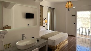 Quarto de hotel moderno com uma cama grande, banheiro com pia e espelho, televisão e varanda com cadeiras.