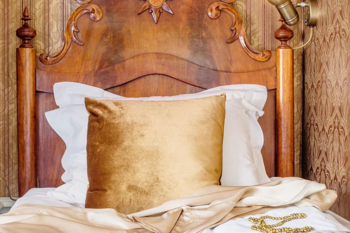A bed with a wooden headboard, a gold pillow, and a floral bedspread.