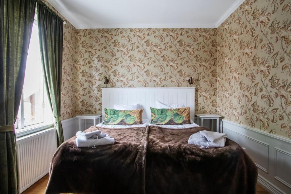A double bed with a brown bedspread and two pillows with a green and brown pattern.