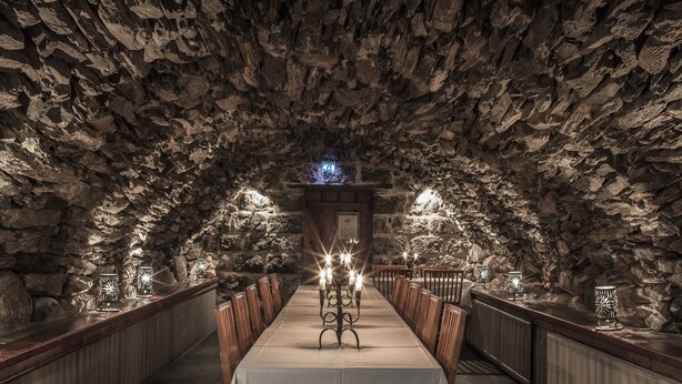 A stone-walled tunnel with a wooden bench and a table in the center, lit by candles and lamps. - Grythyttans Gästgivaregård (Grythyttan)