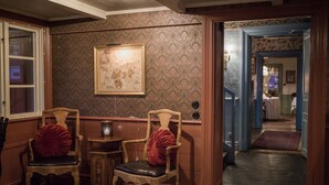 A room with patterned wallpaper, two wooden chairs with red cushions, a small table, and a framed picture on the wall. - Grythyttans Gästgivaregård (Grythyttan)