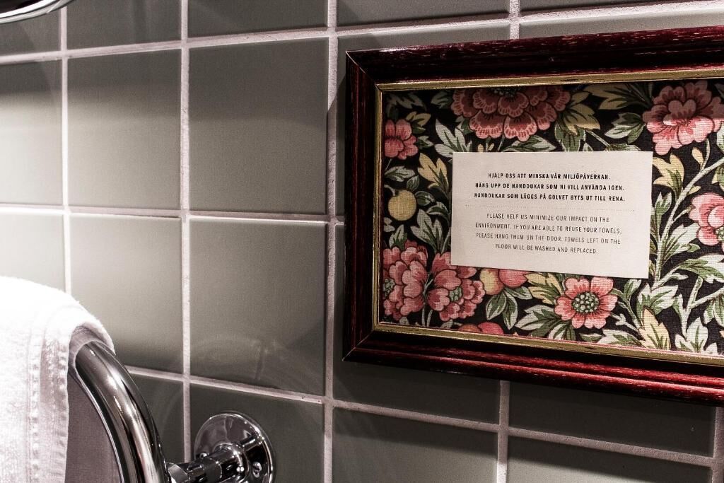 A framed message on a tiled wall, a towel, and a chrome faucet.