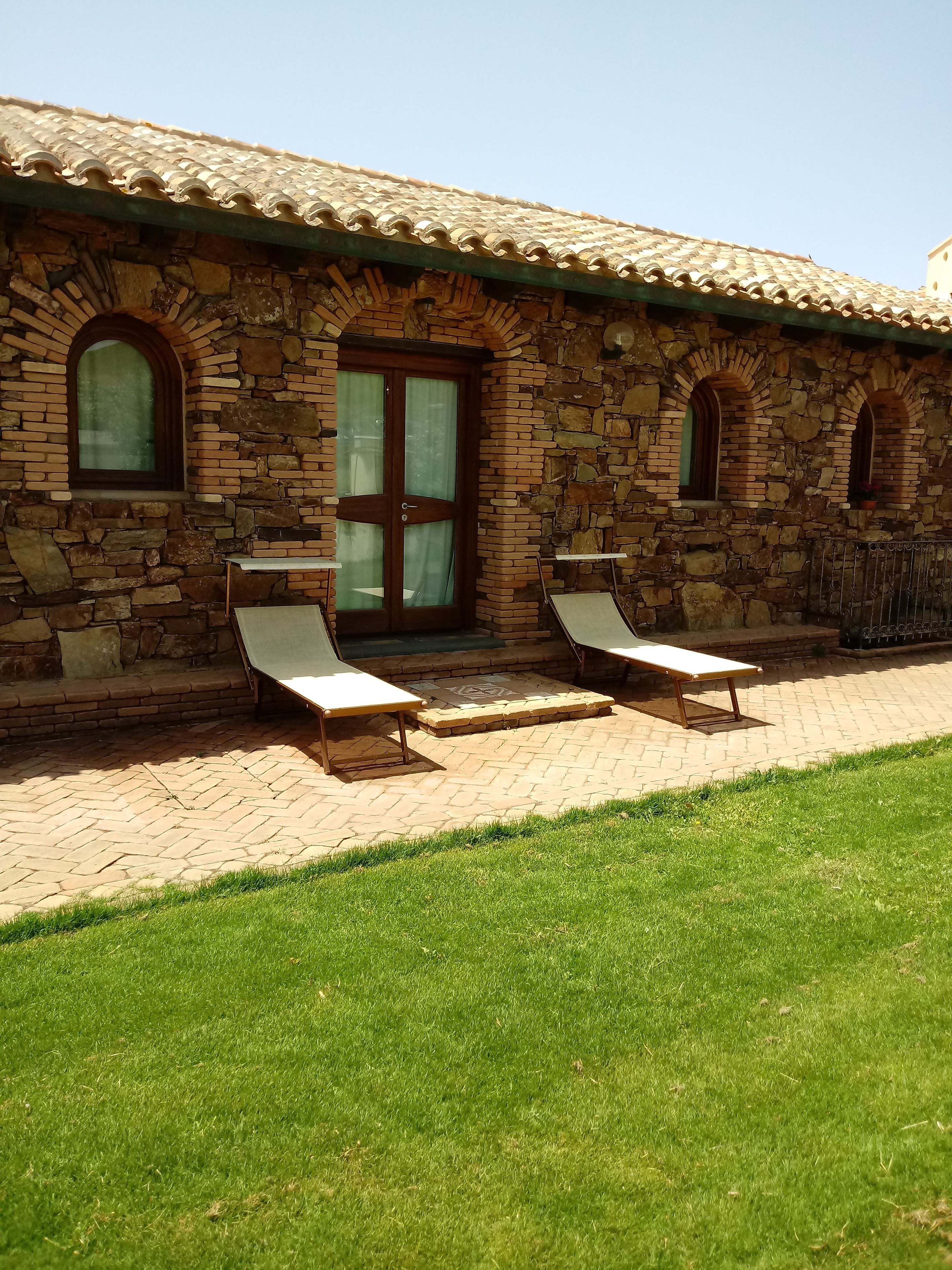 A stone building with a tiled roof, two lounge chairs, and a grassy area in front.