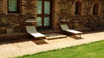 A stone building with a tiled roof, two lounge chairs, and a grassy area in front.