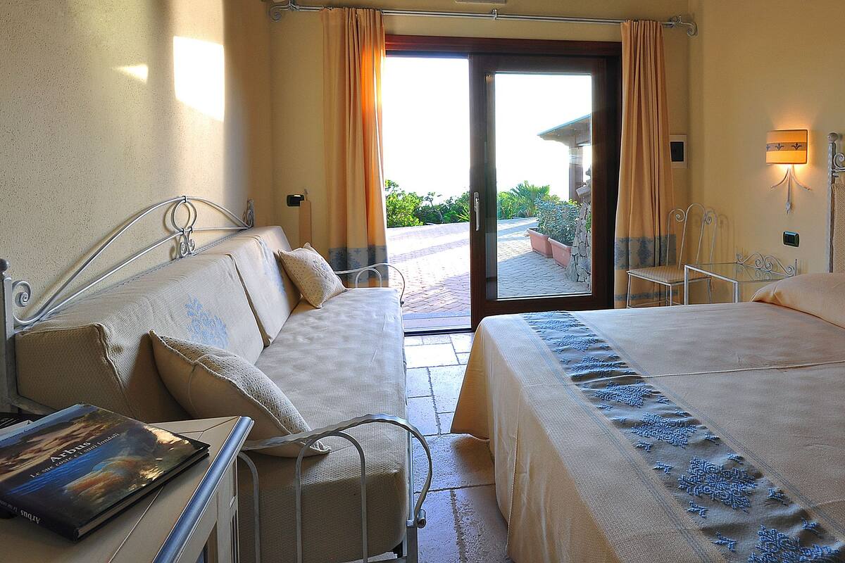 A hotel room with a bed, a sofa, a small table, and a window with curtains.