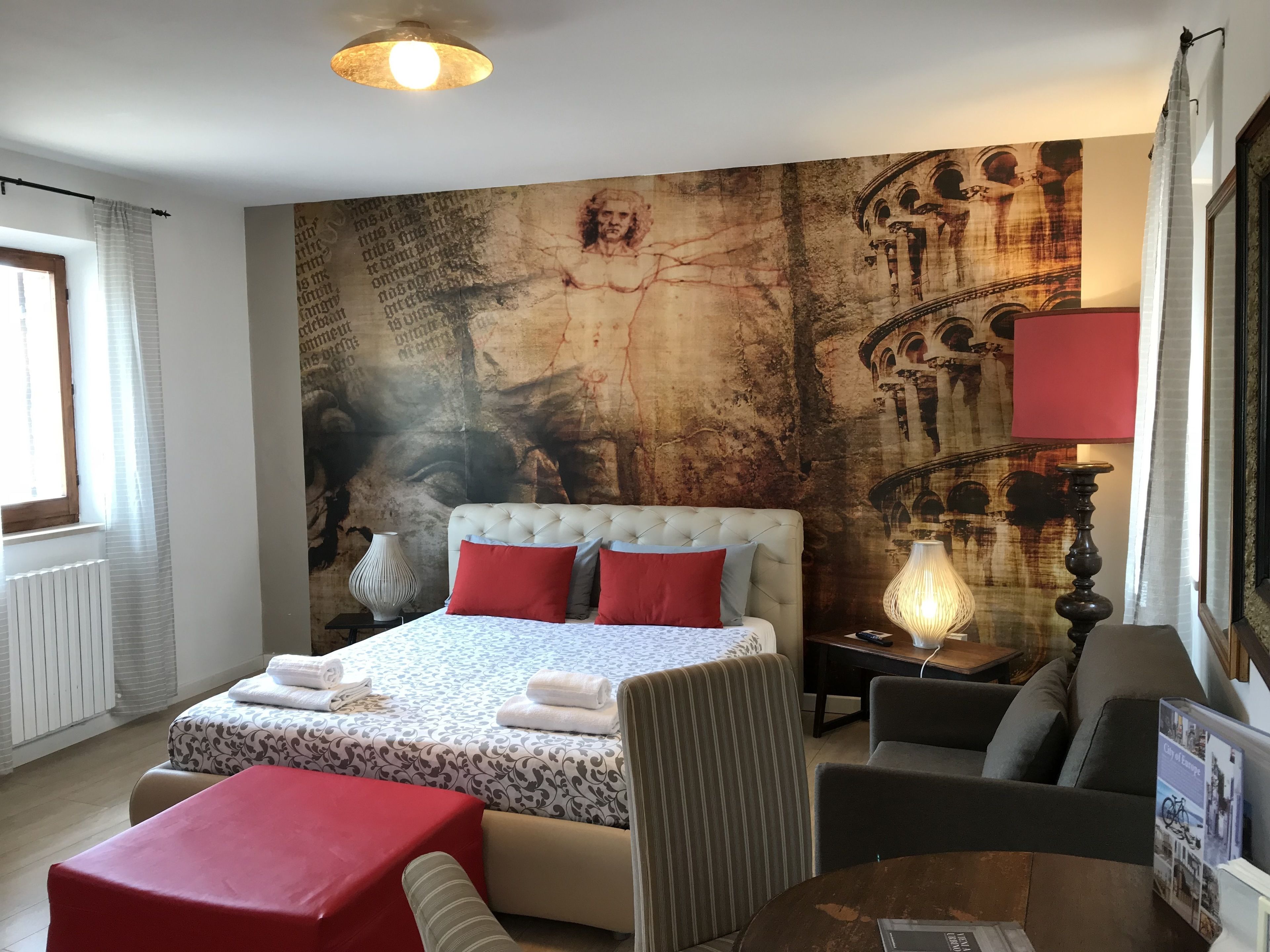 Una habitación de hotel con una cama grande, una zona de estar con una mesa y una pared con un cuadro de gran tamaño.