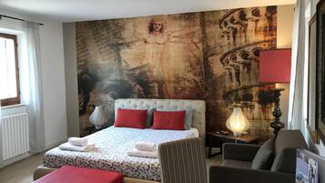 Una habitación de hotel con una cama grande, una zona de estar con una mesa y una pared con un cuadro de gran tamaño.