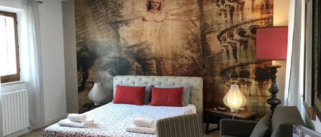 A hotel room with a large bed, a sitting area with a table, and a wall with a large painting.