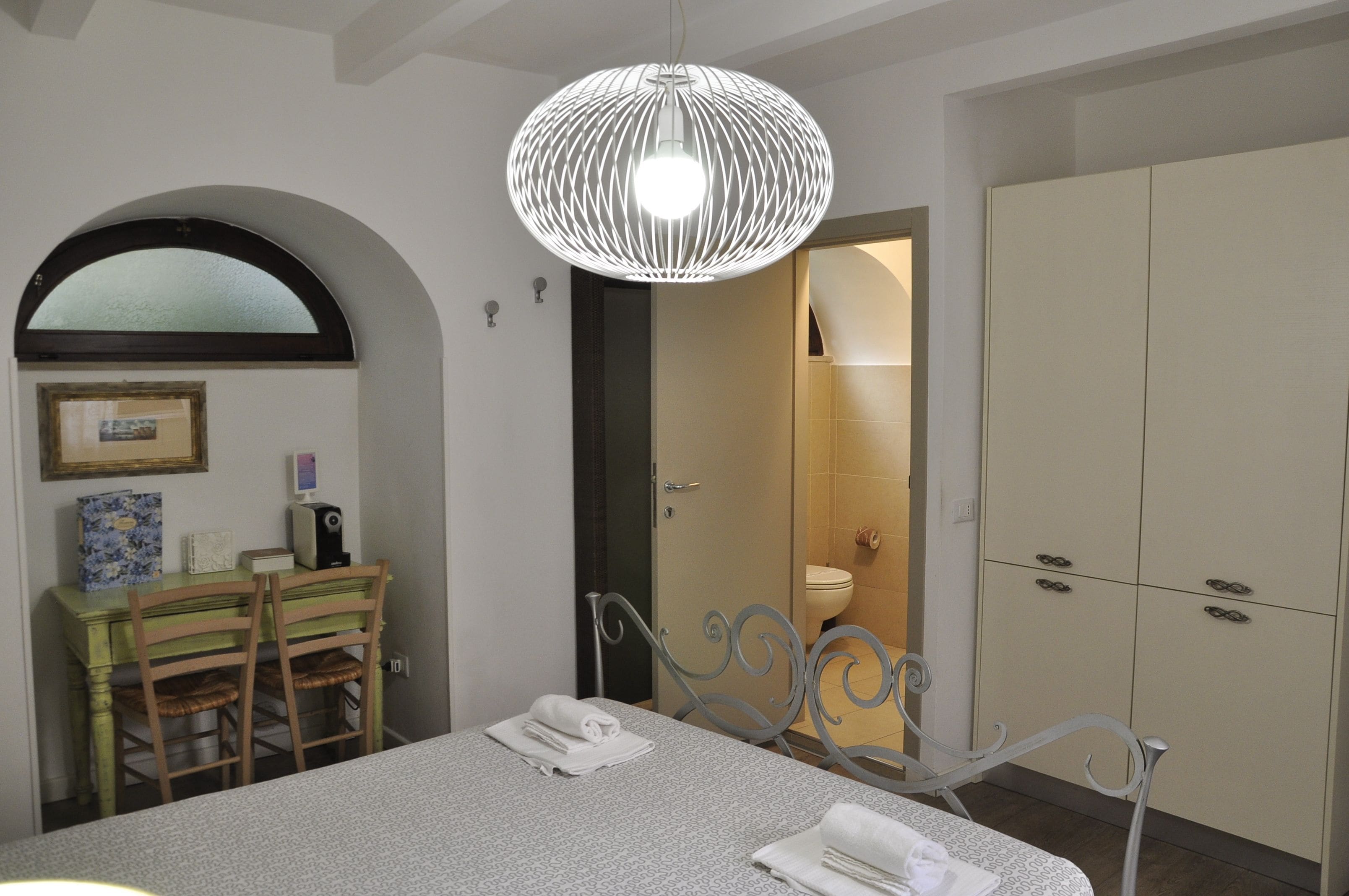 Une chambre d’hôtel avec un lit, une table à manger avec des chaises, une armoire blanche et une salle de bain visible à travers une arche.