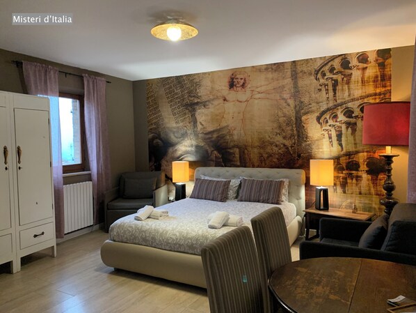 Habitación de hotel con una cama grande, dos mesitas de noche con lámparas, una silla, una pequeña mesa y un armario.