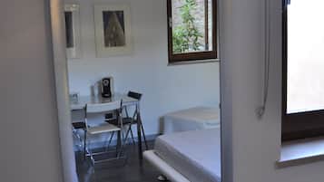 Un dormitorio con una cama, un escritorio y una silla. Se ve follaje verde a través de la ventana.