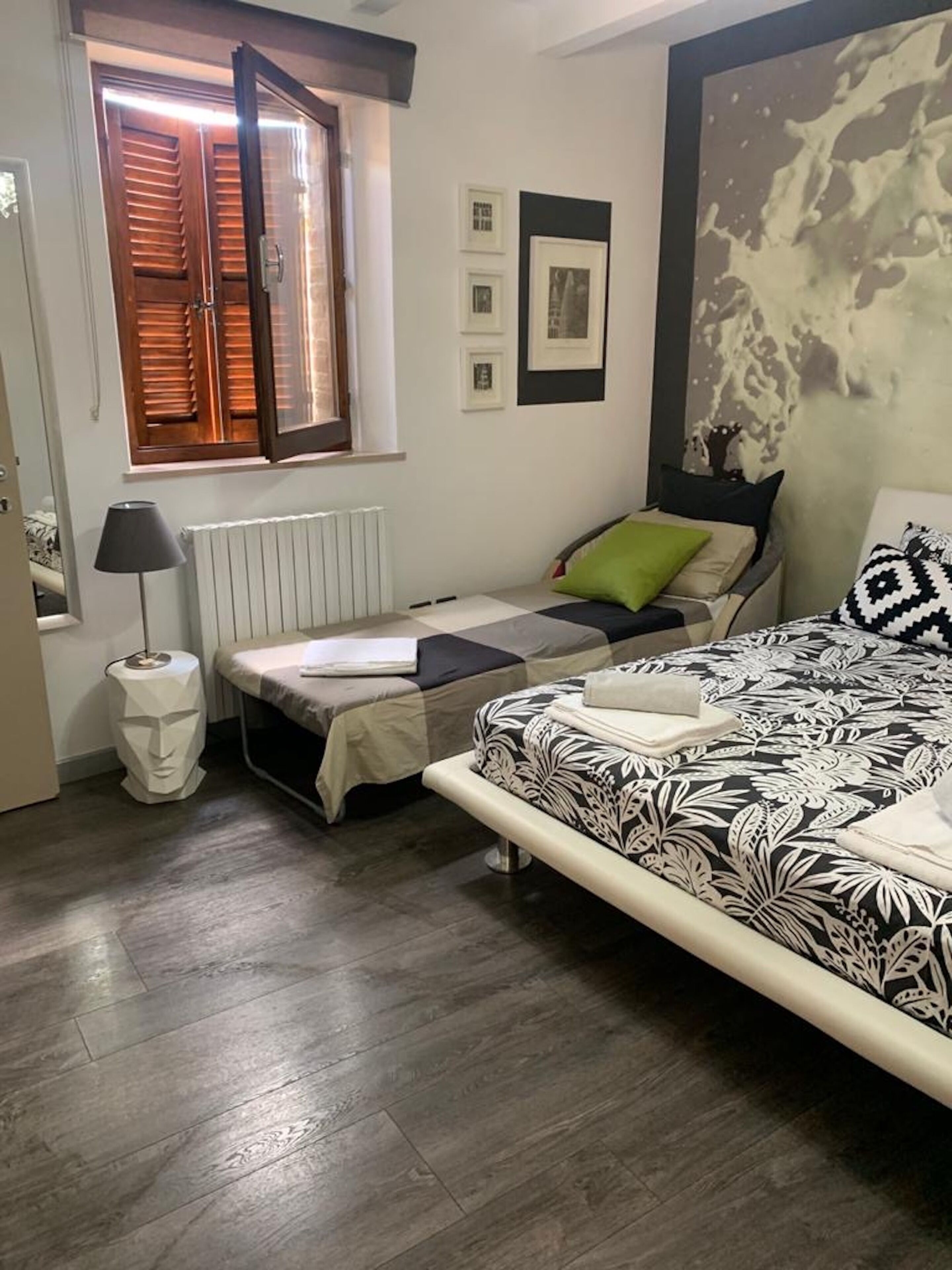 Un dormitorio con dos camas, un radiador, una ventana con persianas y una pared decorada con cuadros.