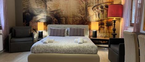 Un dormitorio con una cama grande, dos mesitas de noche con lámparas, una silla y una pared con un mural.