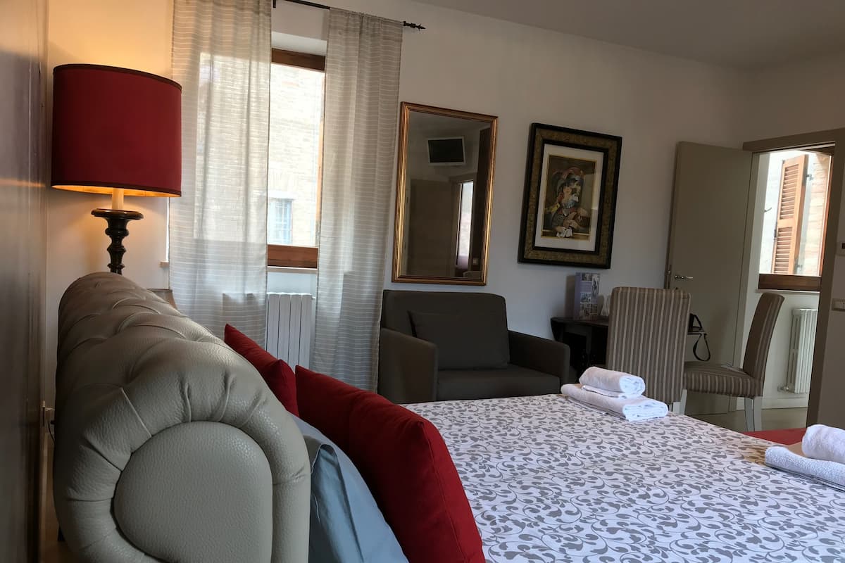 A hotel room with a large bed, a sitting area with chairs, a lamp, a framed picture, and a window with curtains.