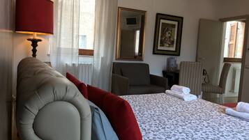A hotel room with a large bed, a sitting area with chairs, a lamp, a framed picture, and a window with curtains.