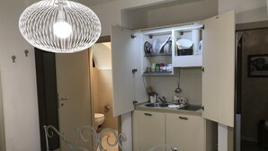 A compact kitchen with a built-in sink, a hanging light fixture, and a small dining area with a metal chair and table. - B&B Albornoz (Urbino)