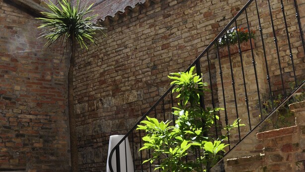 A courtyard with a brick building, a staircase, and potted plants. - B&B Albornoz (Urbino)