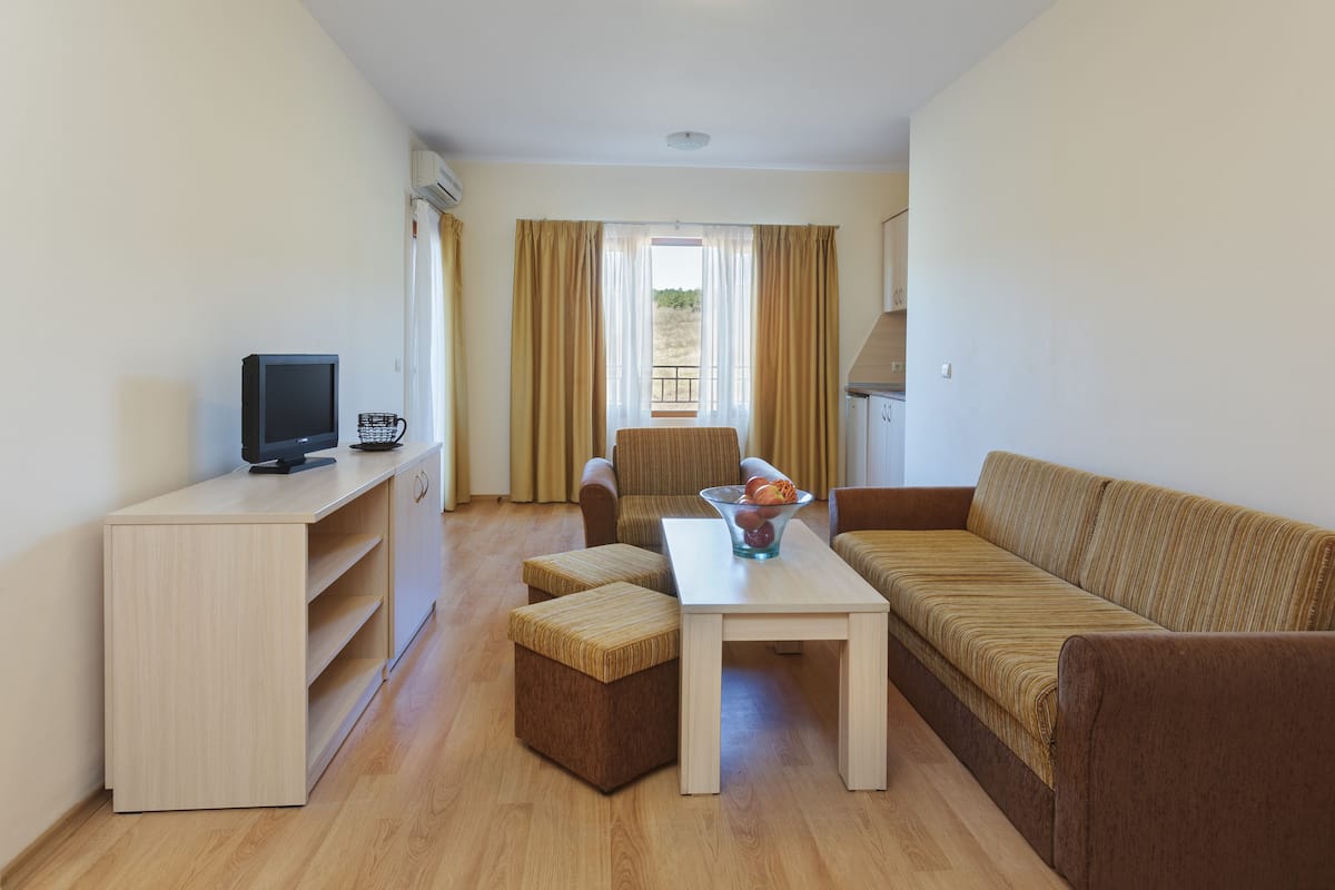 A modern living room with a sofa, a coffee table, a TV, and a small table with a bowl of fruit.