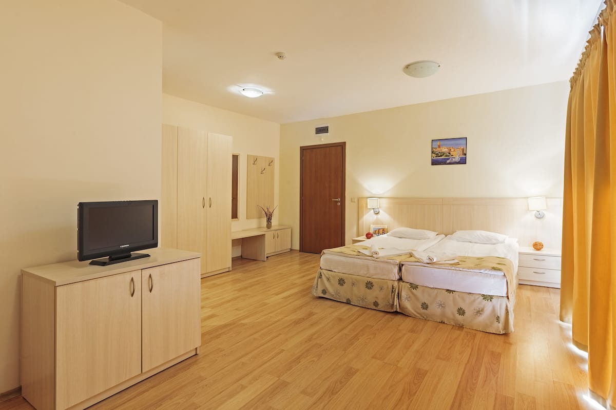 A hotel room with a bed, a TV on a stand, a wardrobe, and a painting on the wall.