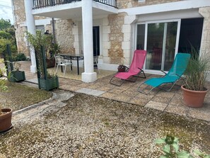 A patio area with a table and chairs, a pink and a blue lounge chair, and potted plants.