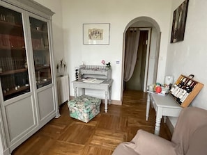 Een woonkamer met een houten vloer, een witte fauteuil, een tafel met een dienblad vol flessen en een boekenkast.