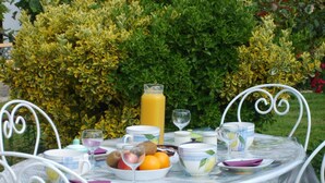 A table set outdoors with a variety of fruits, a glass of orange juice, and a pitcher of water.