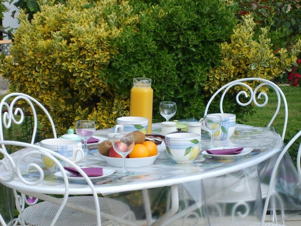 Een buitentafel gedekt met diverse soorten fruit, een glas sinaasappelsap en een waterkan.