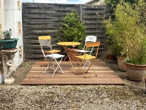 A patio with a wooden table and two chairs, surrounded by gravel and potted plants.