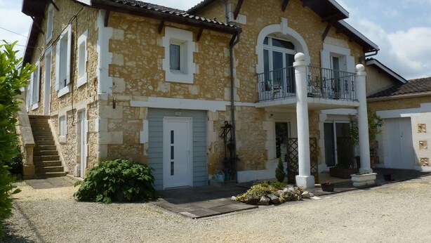 A two-story stone house with a balcony, a front door, and a staircase leading to the entrance.