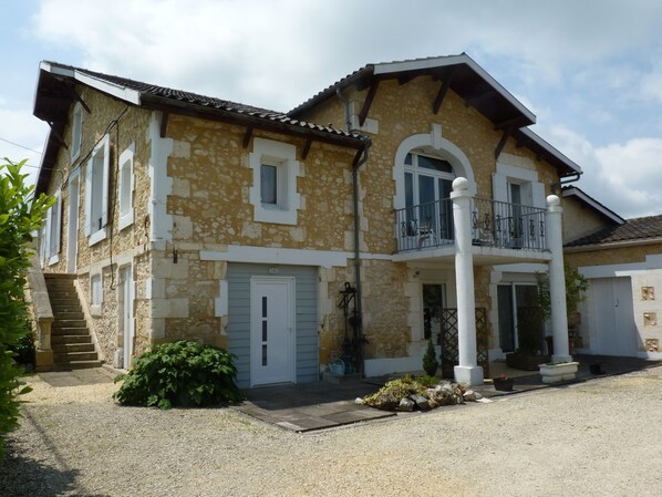 A two-story stone house with a balcony, a front door, and a staircase leading to the entrance. - Le Châlet des Vignes (Saint-Laurent-des-Vignes)