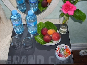 Een tafel met waterflesjes, een schaal fruit, een vaas met een roze bloem en een kom met snoep.