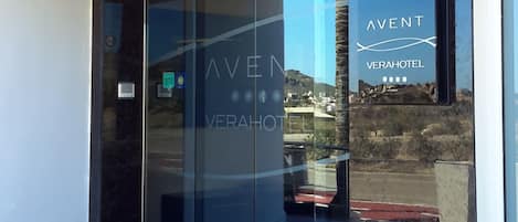 A modern hotel entrance with a glass door, a clear view of the surrounding area, and a sign indicating the hotel name.
