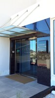Una entrada de hotel moderna con puerta de cristal, vista despejada del entorno y un cartel con el nombre del hotel.