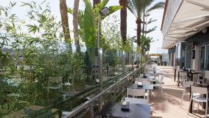 An outdoor dining area with tables and chairs, surrounded by glass railings and greenery.
