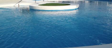 A swimming pool with a central circular area, surrounded by lounge chairs and umbrellas.